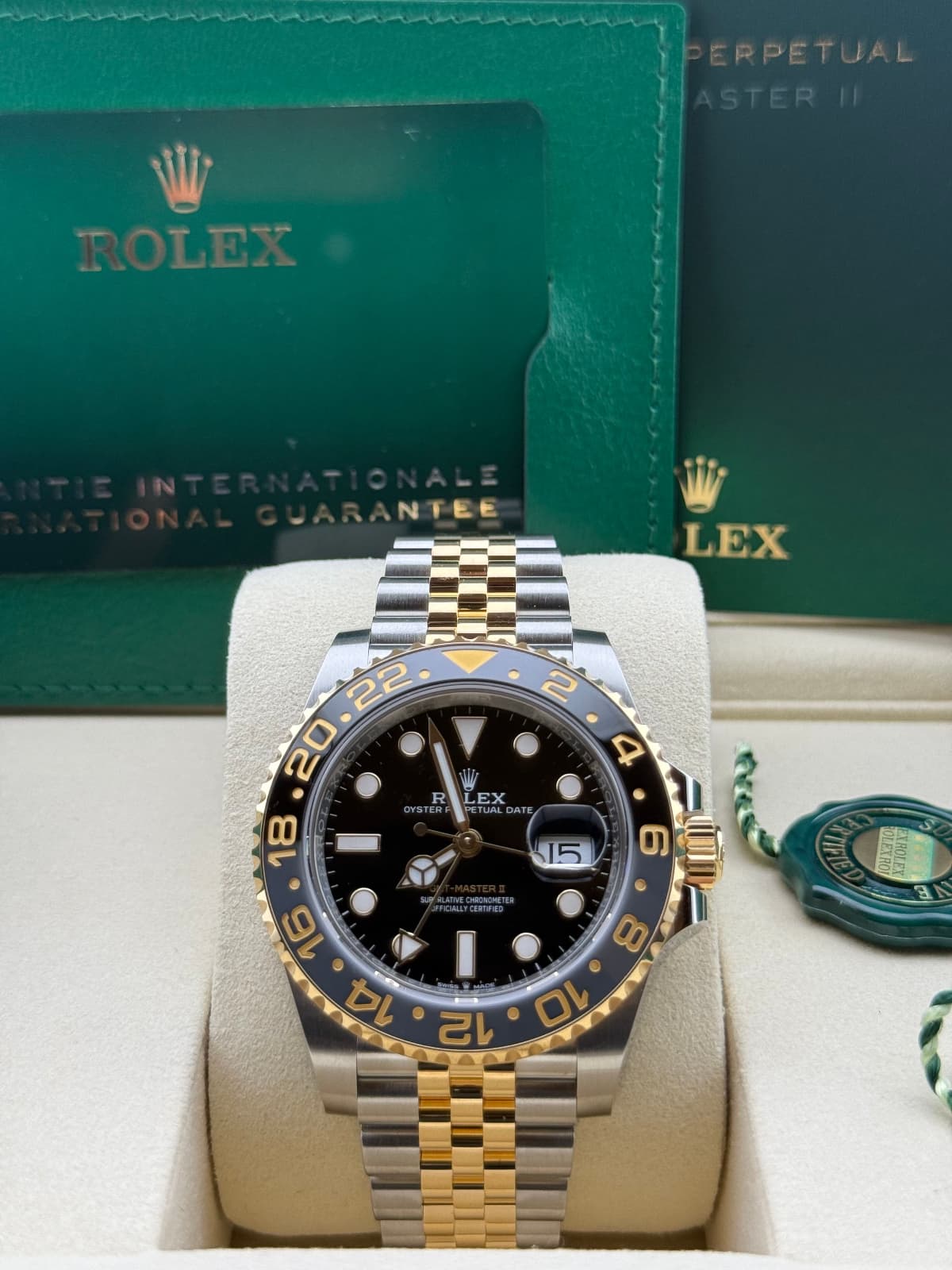 Rolex GMT-Master Yellow Gold/Stainless steel 126713GRNR – watch with black dial and gold bezel on a white stand, with a green box featuring Rolex branding in the background.