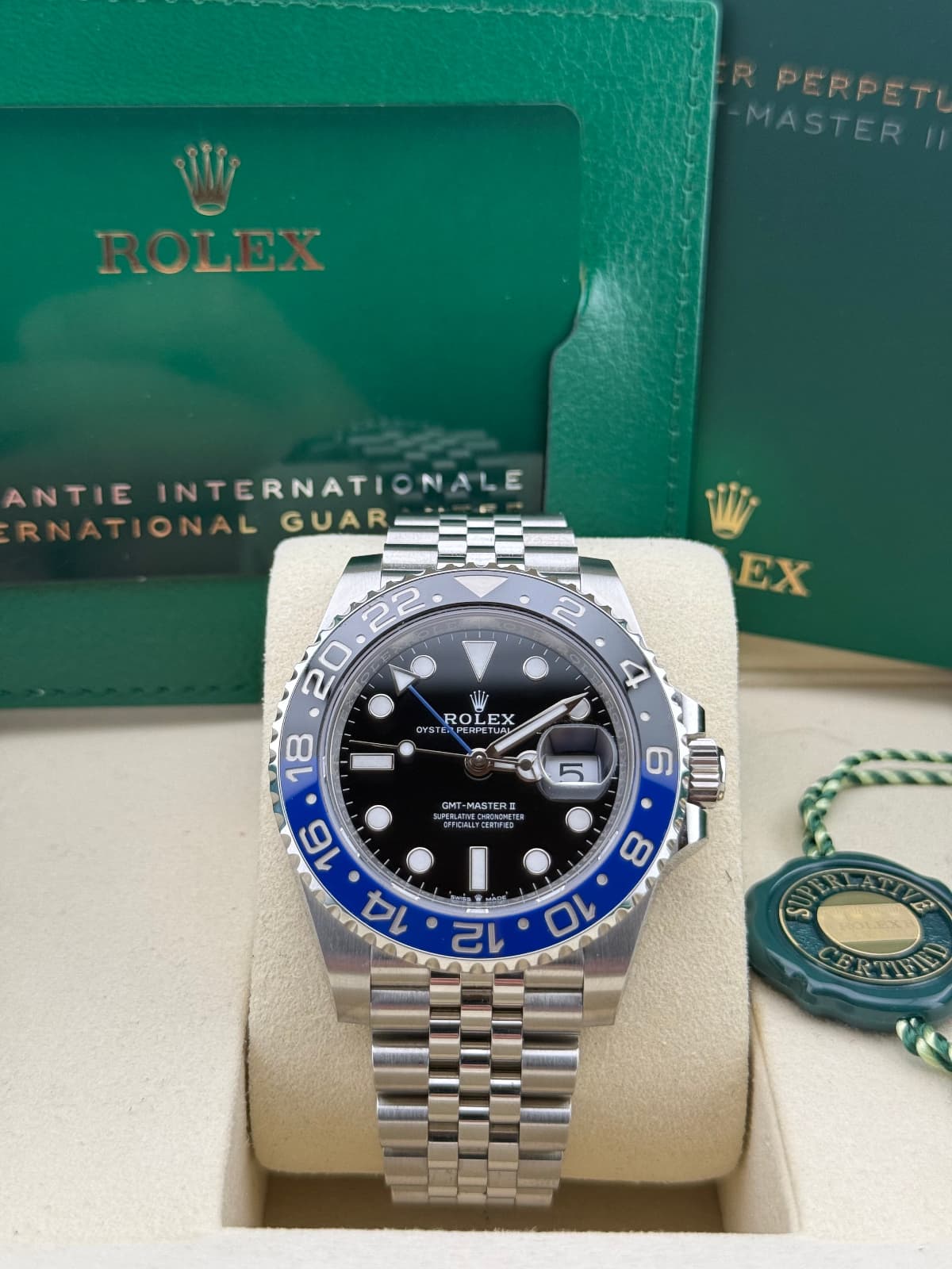 Rolex GMT-Master “Batgirl” Jubilee 126710BLNR – watch with blue and black bezel on a white cushion, with green Rolex box in the background.