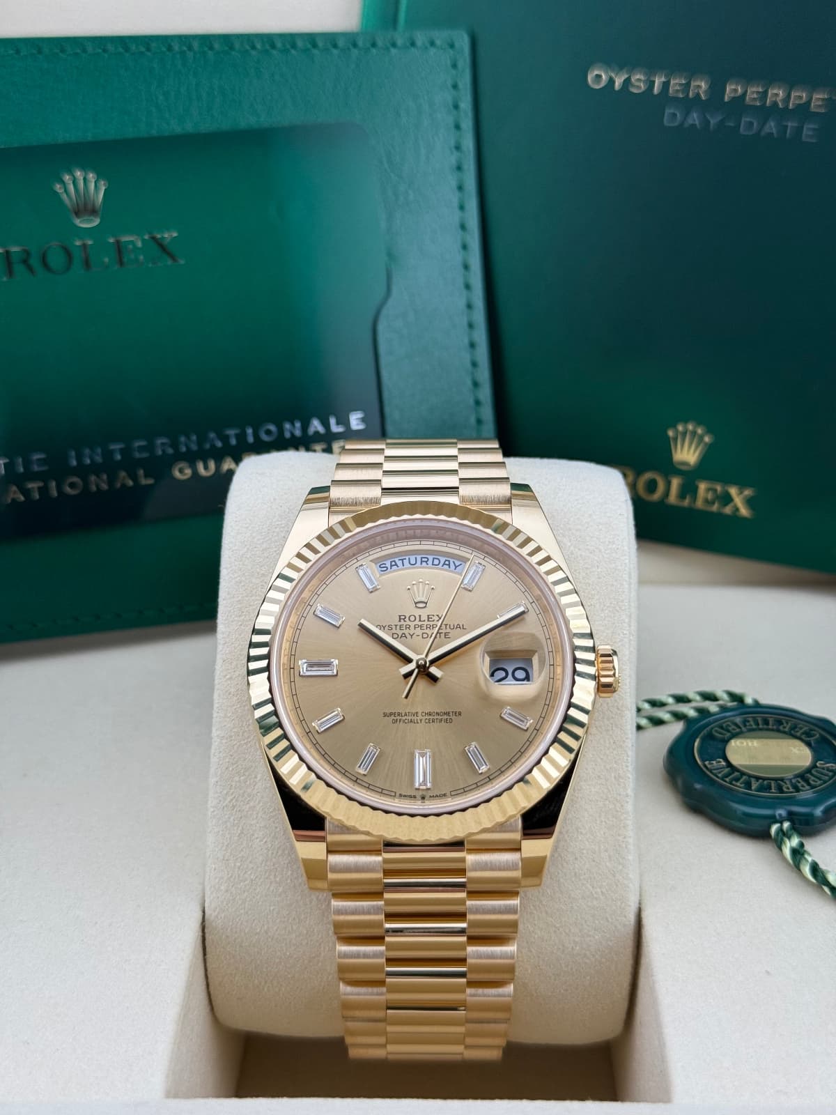 Rolex Day-Date 40 Champagne Baguette 228238 – Gold Rolex watch in a box with a green Rolex box in the background