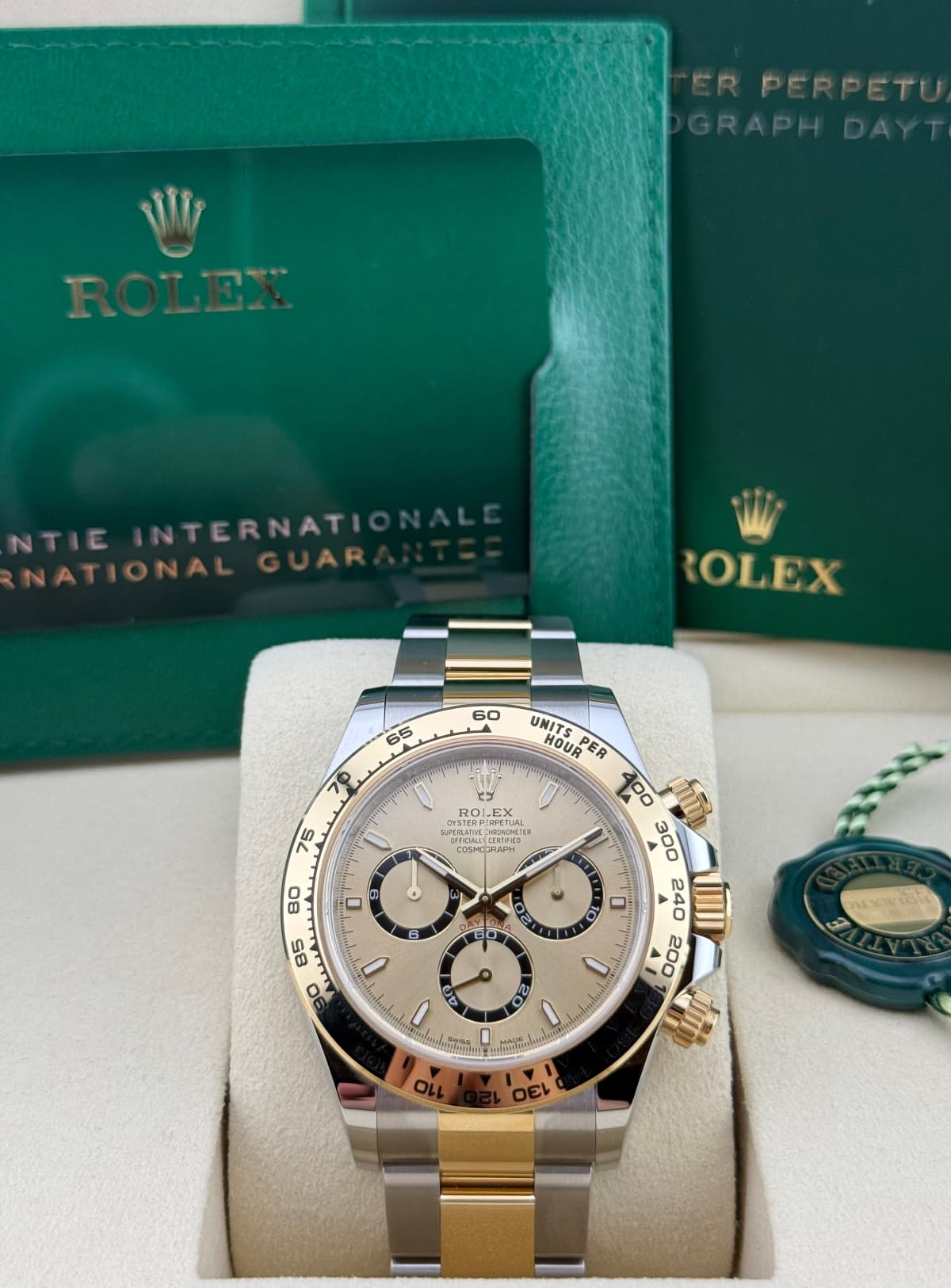 Rolex Daytona Champagne Yellow Gold/Steel 126503 - watch with gold and silver band on a white cushion, with a green Rolex box in the background.